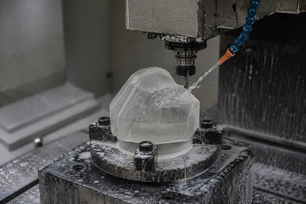 A CNC machine pre-shaping a crystal block into a basic form before detailed carving.