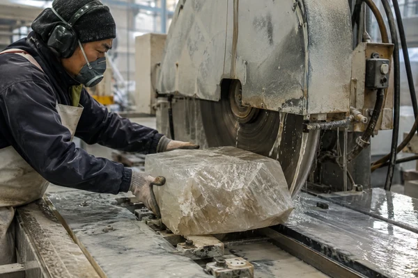 A factory worker using a large diamond saw to cut a raw crystal block, a key step in how crystal carvings are made.
