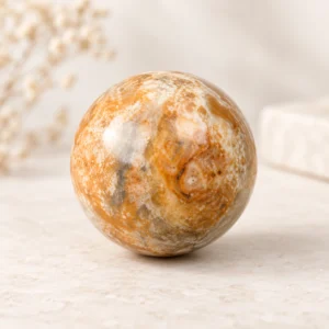 Crazy Lace Agate crystal sphere with warm orange cream and gray natural patterns on a light minimalist tabletop.