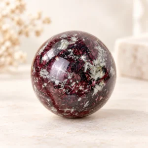 Eudialyte crystal sphere with deep red black and gray natural mineral patterns on a light minimalist tabletop.