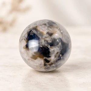 Gray and white polished crystal sphere with blue mineral inclusions on a soft beige background