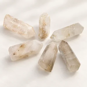 Six polished clear crystal towers displayed in a clean minimalist still life on a soft cream background.