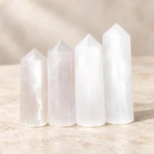 Four polished white crystal towers displayed on a light beige marble tabletop in a minimalist product photography scene.