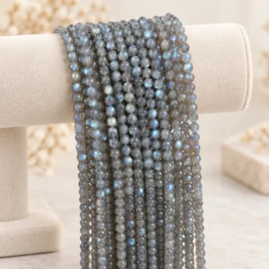 Grey-blue labradorite bead strands draped over a cream velvet jewelry display on a light beige tabletop.