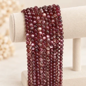 Deep burgundy round gemstone bead strands arranged over a cream velvet display stand in a minimalist setting.