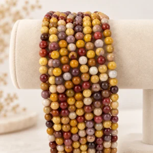 Warm-toned round gemstone bead strands in yellow, cream, tan, and red shades displayed on a cream velvet stand.