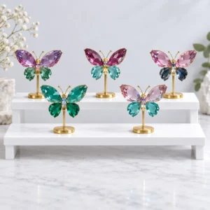 Crystal butterfly ornaments in mixed colors displayed on elegant gold stands in a bright studio scene.