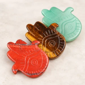 Red, tiger eye and green evil eye palm crystal carvings arranged on a light minimalist tabletop