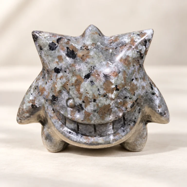Fire quartz ghost monster crystal carving with natural speckled stone texture on a light minimalist tabletop
