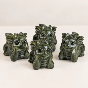 Green jade baby dragon crystal carvings with carved spikes and round eyes on a light minimalist tabletop
