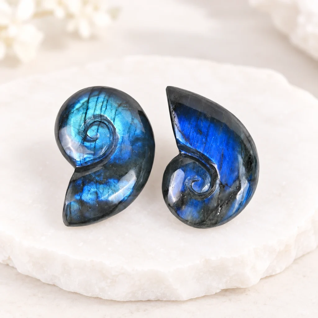 Pair of labradorite conch shell crystal carvings with vivid blue flash on a light minimalist tabletop