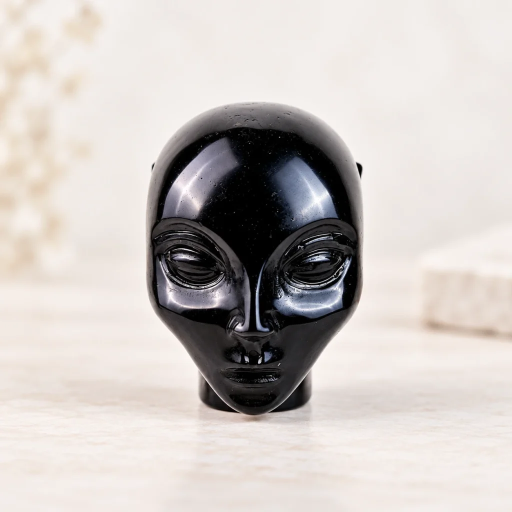 Obsidian Alien Head Crystal Carving on a light minimalist tabletop background