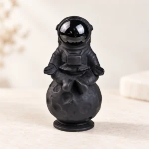 Obsidian Astronaut Crystal Carving on a light minimalist tabletop background
