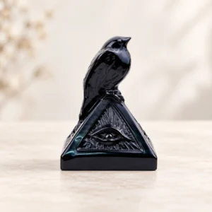 Obsidian Crow with Pyramid Crystal Carving on a light minimalist tabletop background