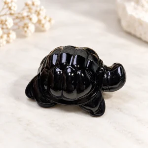 Glossy black obsidian sea turtle crystal carving on a light minimalist tabletop