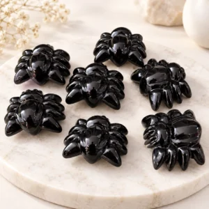 Glossy black obsidian spider crystal carvings arranged on a light minimalist tabletop