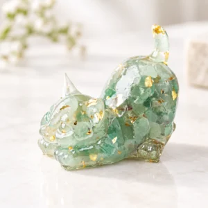 Pale green playful cat crystal carving with translucent stone and gold fleck details on a light tabletop