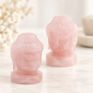 Pair of rose quartz Buddha head crystal carvings in soft translucent pink on a light minimalist tabletop