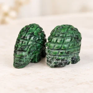 Pair of ruby zoisite pangolin crystal carvings with green and black natural stone patterns on a light minimalist tabletop
