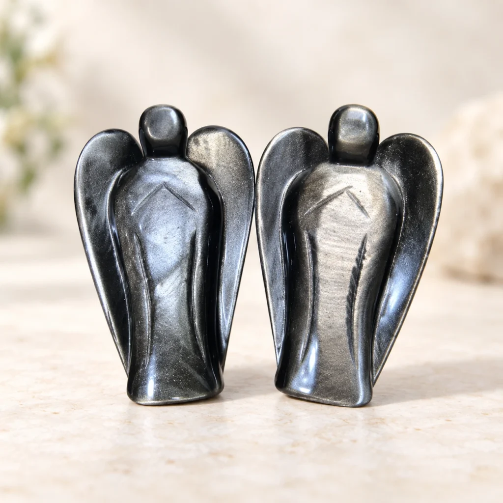 Pair of silver sheen obsidian angel crystal carvings with reflective gray black wings on a light minimalist tabletop
