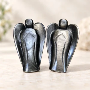 Pair of silver sheen obsidian angel crystal carvings with reflective gray black wings on a light minimalist tabletop