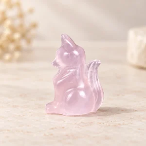 Pink translucent sitting fox crystal carving with raised tail on a light minimalist tabletop