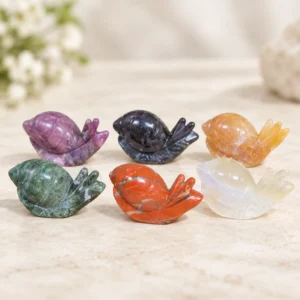 Assorted natural crystal snail carvings in green red purple orange black and white on a light minimalist tabletop