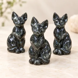 Three dark natural stone Sphynx cat crystal carvings arranged on a light minimalist tabletop