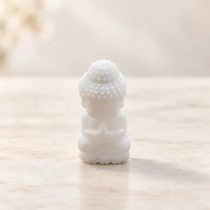 White marble baby Buddha crystal carving in a seated prayer pose on a light minimalist tabletop