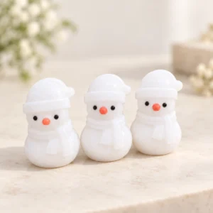 Three white marble snowman crystal carvings with black eyes and orange noses on a light minimalist tabletop