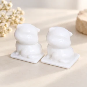 Pair of white marble cat crystal carvings on square bases arranged on a light minimalist tabletop